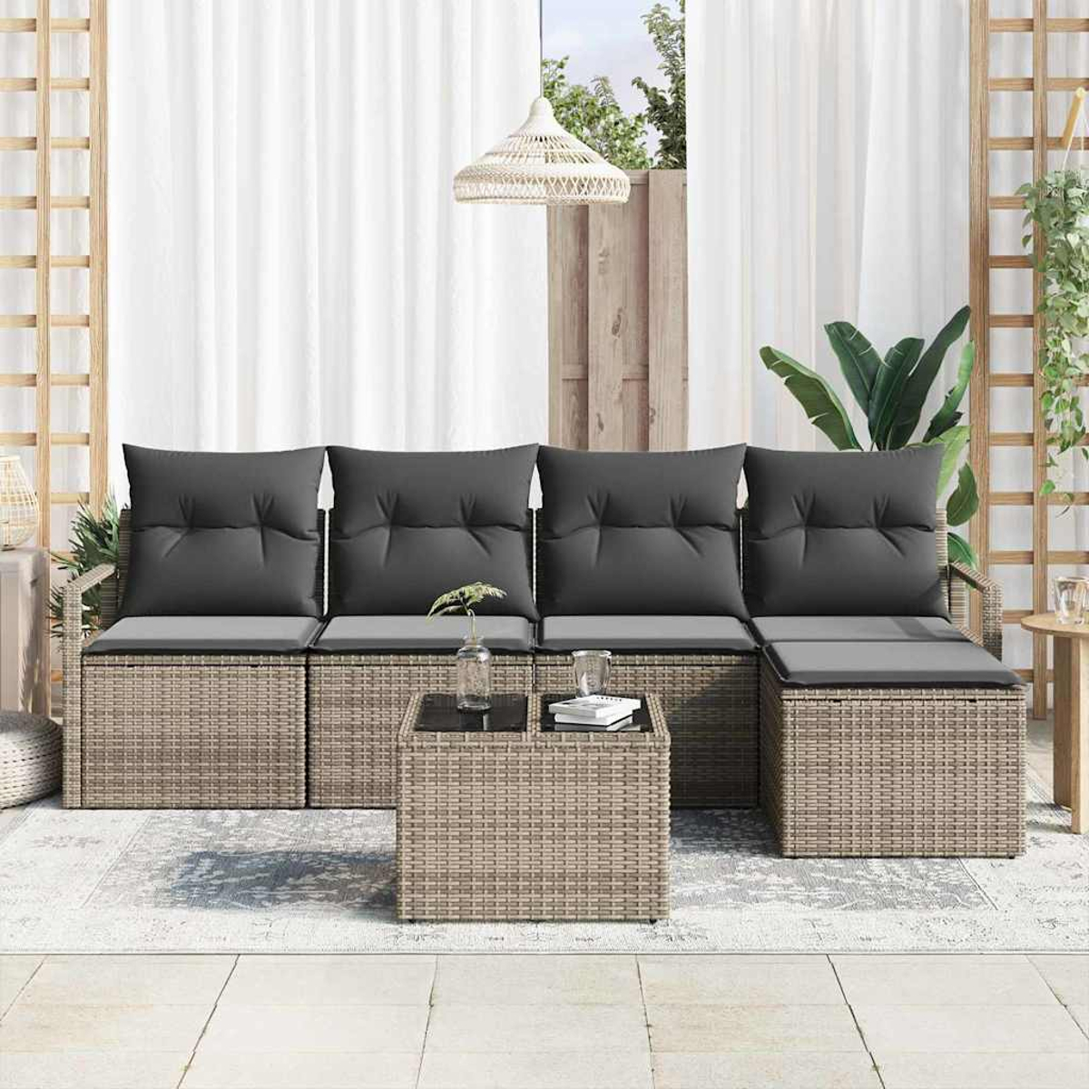 Outdoor-Korbmöbel-Set mit grauen Kissen. Ein Couchtisch mit Gläsern und Büchern befindet sich davor. Weiße Vorhänge im Hintergrund.