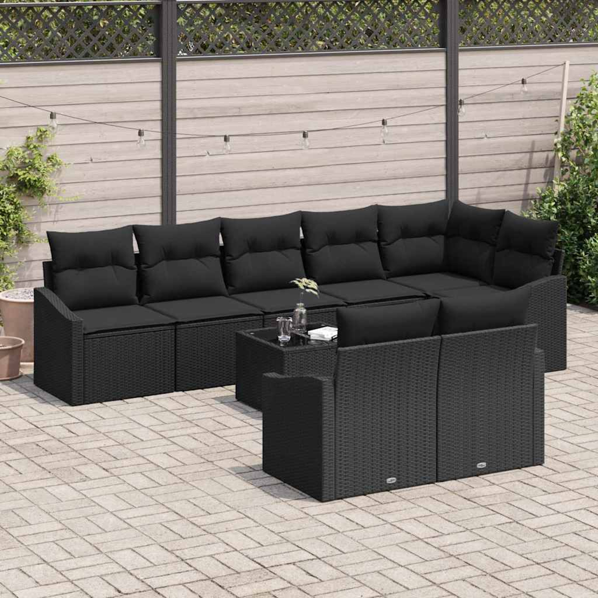 Terrassenmöbel-Set mit schwarzem Korbmöbeln und Kissen. Enthält ein Ecksofa, zwei Stühle und einen Tisch mit Glasplatte auf einer Ziegelterrasse.