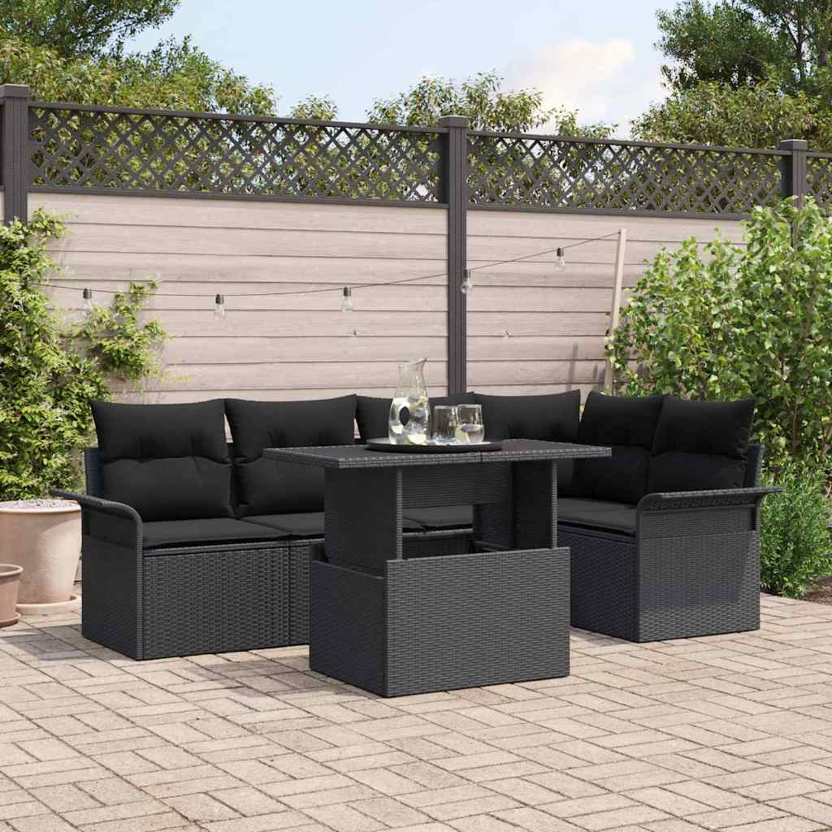 Terrassenset mit schwarzem Sofa, Stühlen und Tisch mit Gläsern. Im Hintergrund ein Zaun und Grün.