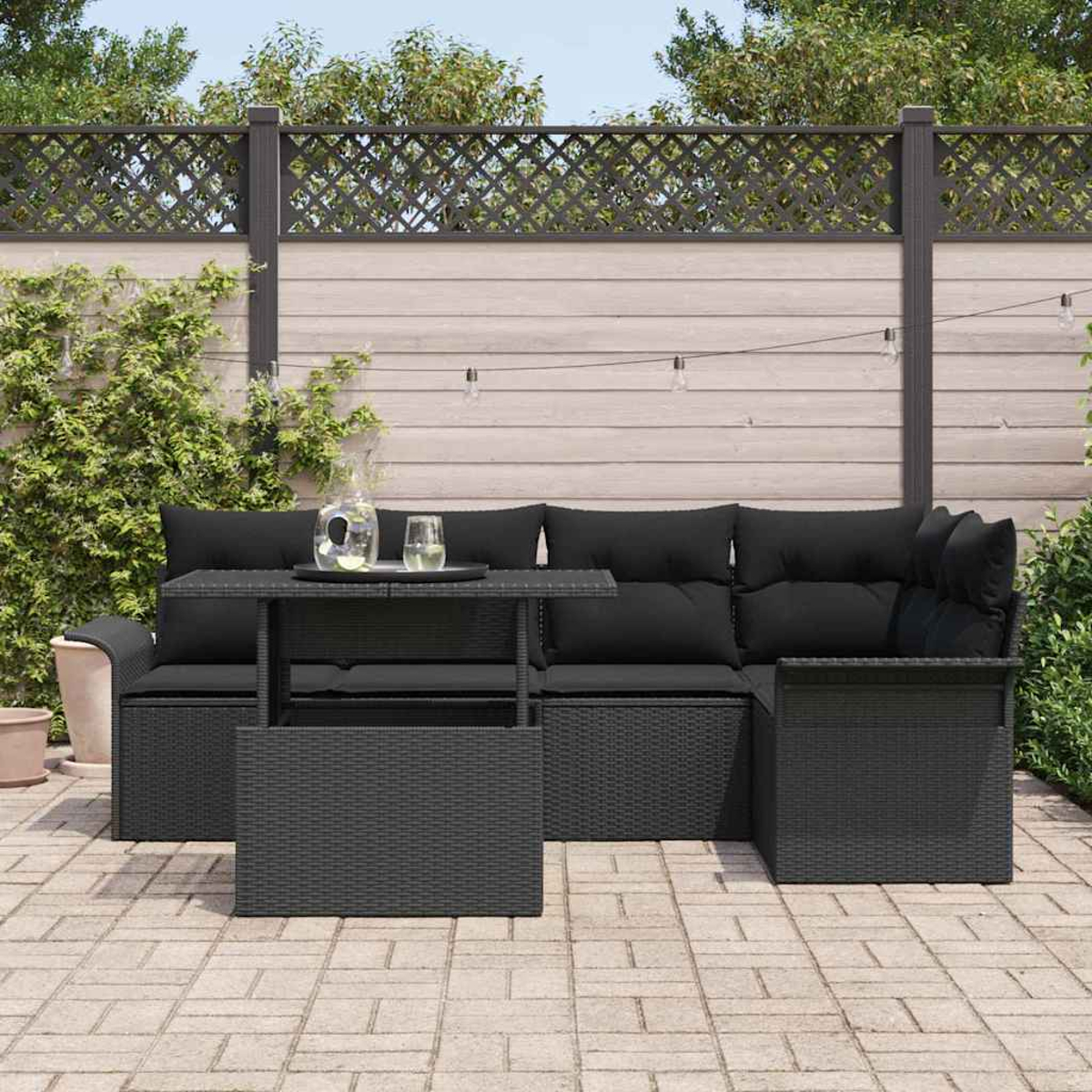 Schwarzes Outdoor-Ecksofa mit Kissen und einem Tisch. Ein Glas Wasser und eine Kanne stehen auf dem Tisch. Im Hintergrund ist ein Zaun zu sehen.