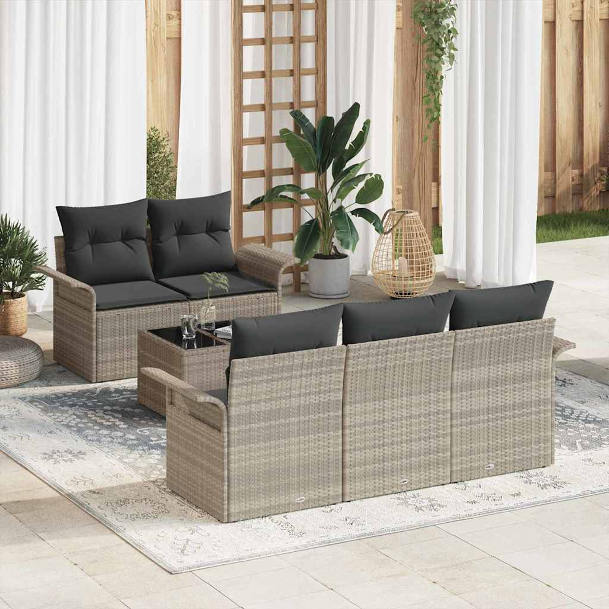 Terrassen-Set mit grauen Kissen. Enthält eine Couch, ein Sofa und einen Couchtisch auf einem gemusterten Teppich, umgeben von Pflanzen.