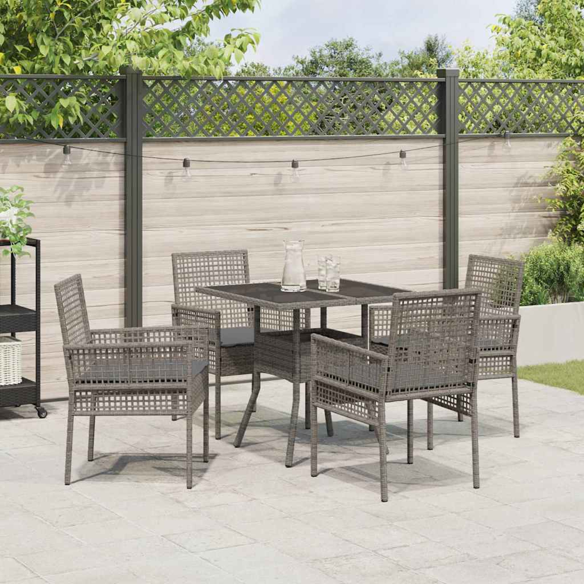 Terrassenset mit grauen Stühlen und einem Tisch. Im Hintergrund befinden sich ein Zaun und Grün. Gläser und ein Krug stehen auf dem Tisch.