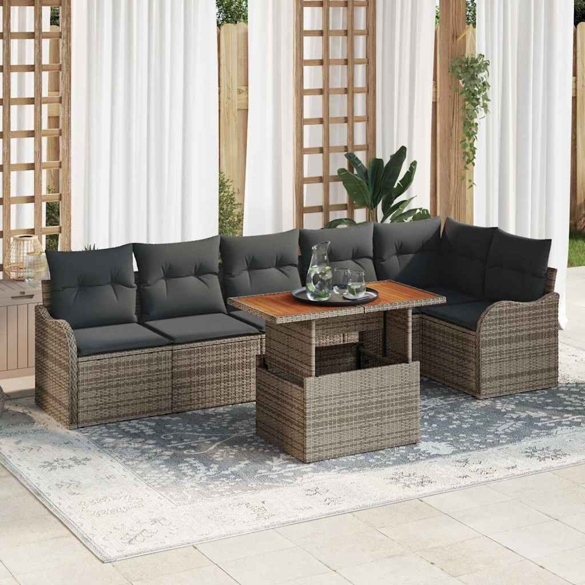 Geflecht-Terrassenmöbel-Set mit grauen Kissen. Ein Tisch mit Holzplatte und ein Teppich stehen vor weißen Vorhängen.