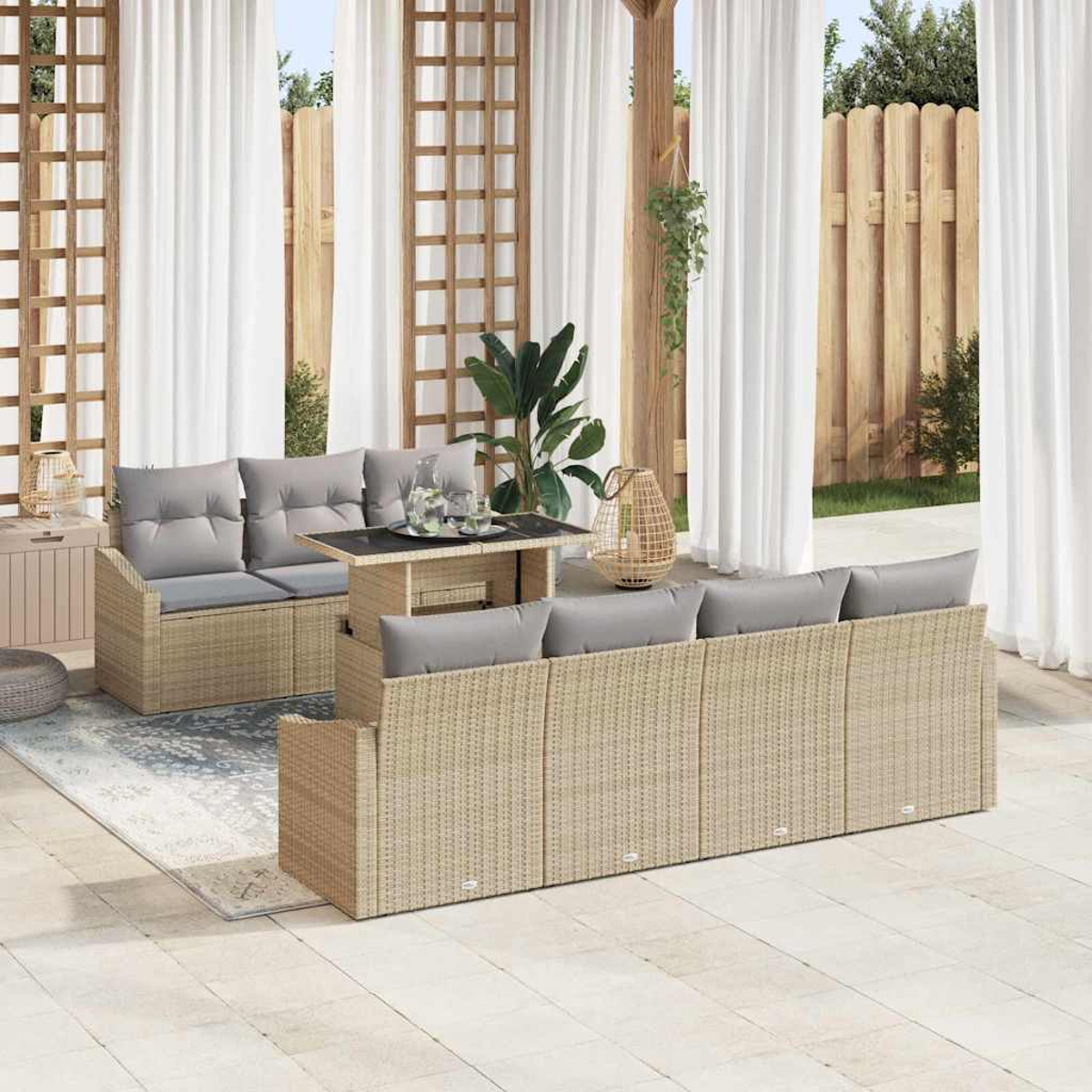 Terrassenset mit beigefarbenen Korbsesseln, grauen Kissen, einem Tisch und weißen Vorhängen. Holzzaun und grüne Pflanzen im Hintergrund.