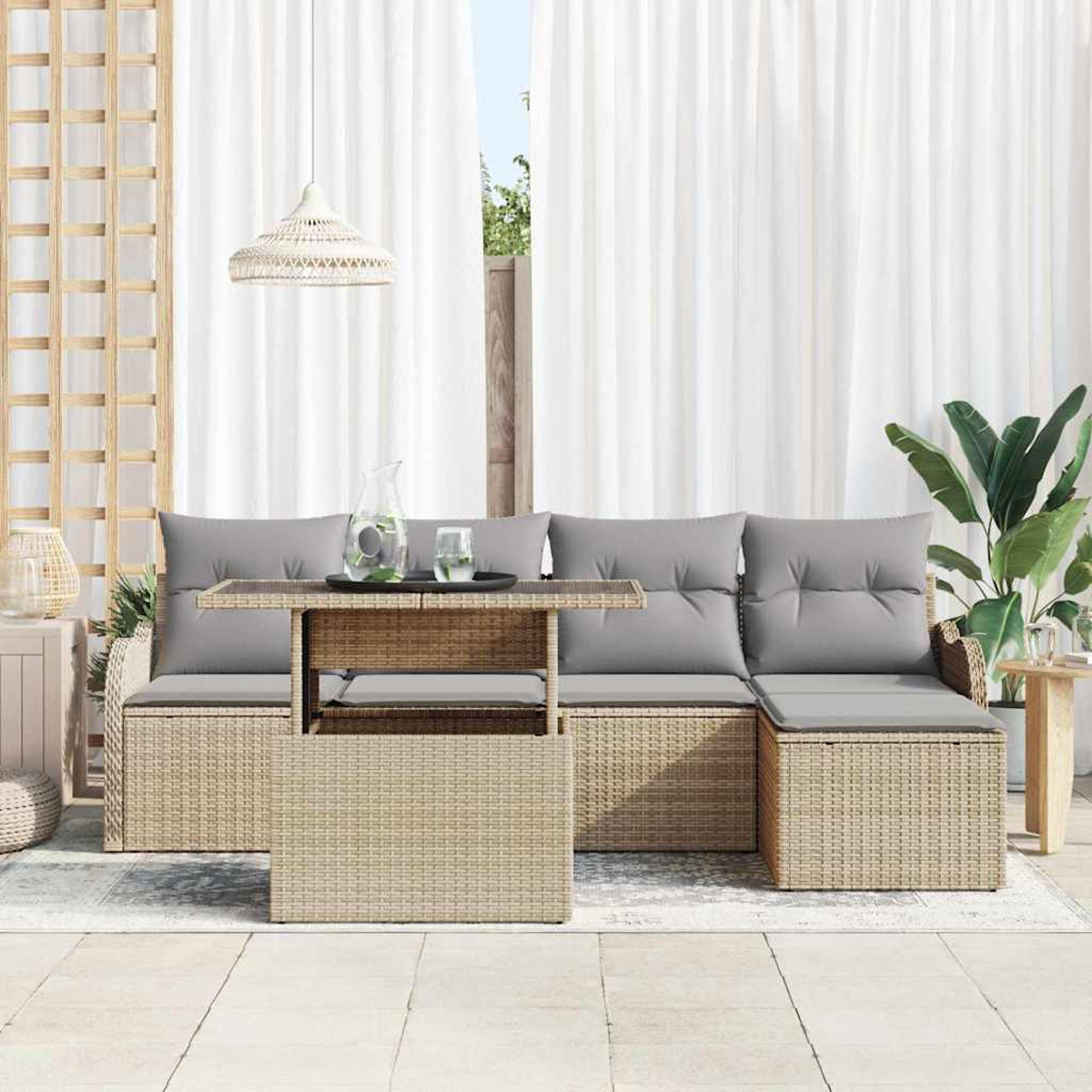 Outdoor-Rattansofa mit grauen Kissen und einem Glastisch. Weiße Vorhänge im Hintergrund, rechts eine Pflanze.