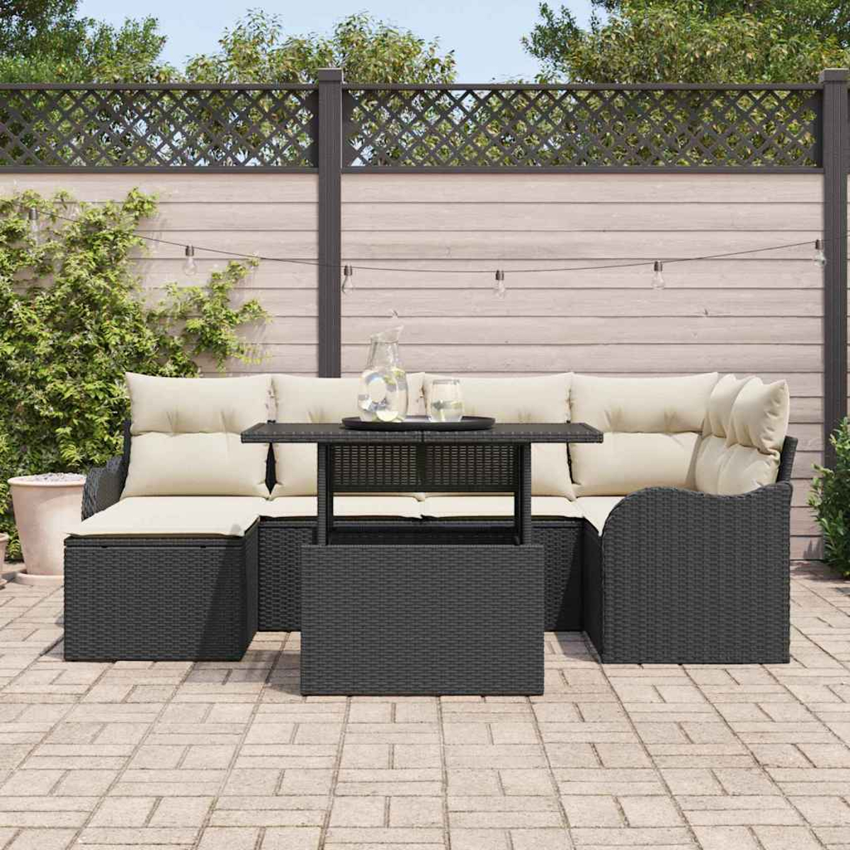 Garten-Sitzgruppe: schwarzes Korbmöbel-Sofa und -Stuhl mit cremefarbenen Kissen, Couchtisch und Glaskrug auf einer Terrasse.