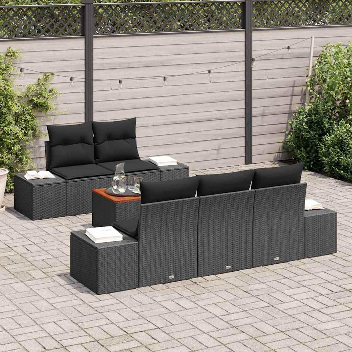Garten-Terrassenset. Dunkelgraue Korbmöbel mit schwarzen Kissen. Enthält ein Sofa, zwei Stühle und einen Couchtisch auf einer gepflasterten Terrasse.