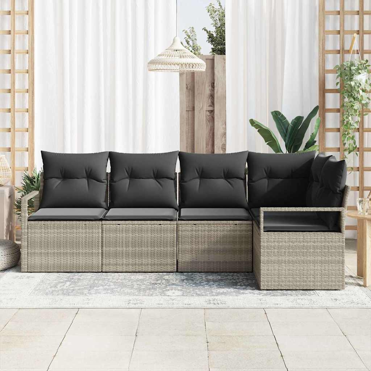 Graues Rattan-Outdoor-Sofa mit dunkelgrauen Kissen steht auf einer gefliesten Terrasse. Weiße Vorhänge und Pflanzen sind im Hintergrund.