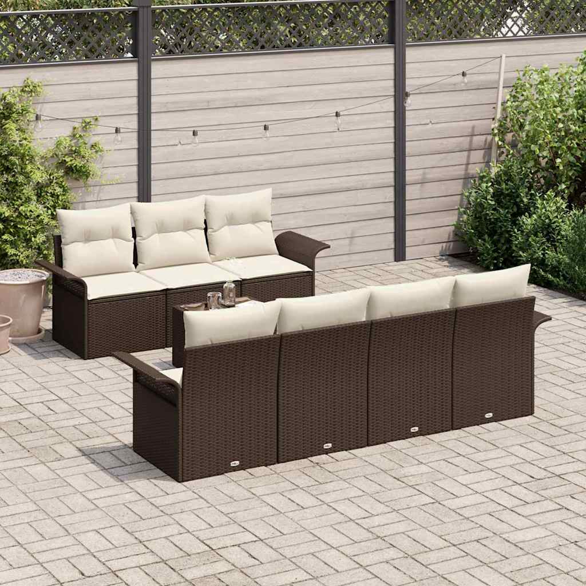 Szene im Freien mit zwei braunen Korbs Sofas mit cremefarbenen Kissen. Im Hintergrund befindet sich ein Holzzaun. Gepflasterte Terrasse.