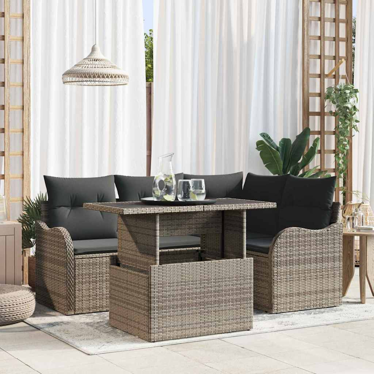 Outdoor-Rattanmöbel-Set mit Tisch und zwei Sofas mit grauen Kissen und weißen Vorhängen im Hintergrund.
