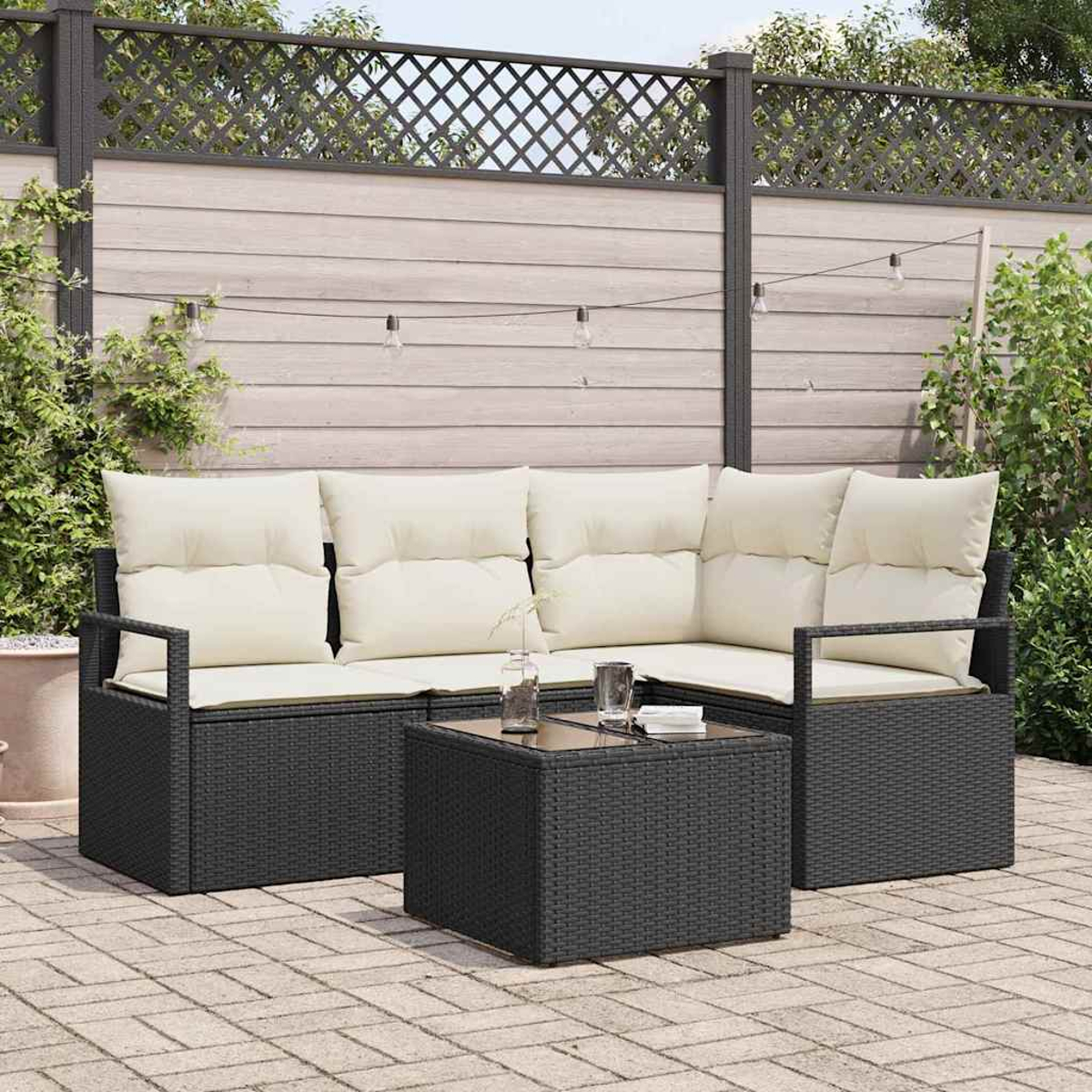 Ein Outdoor-Terrassenset mit einem schwarzen Korbsessel und Couchtisch, beigen Kissen und einem Holzzaun im Hintergrund.