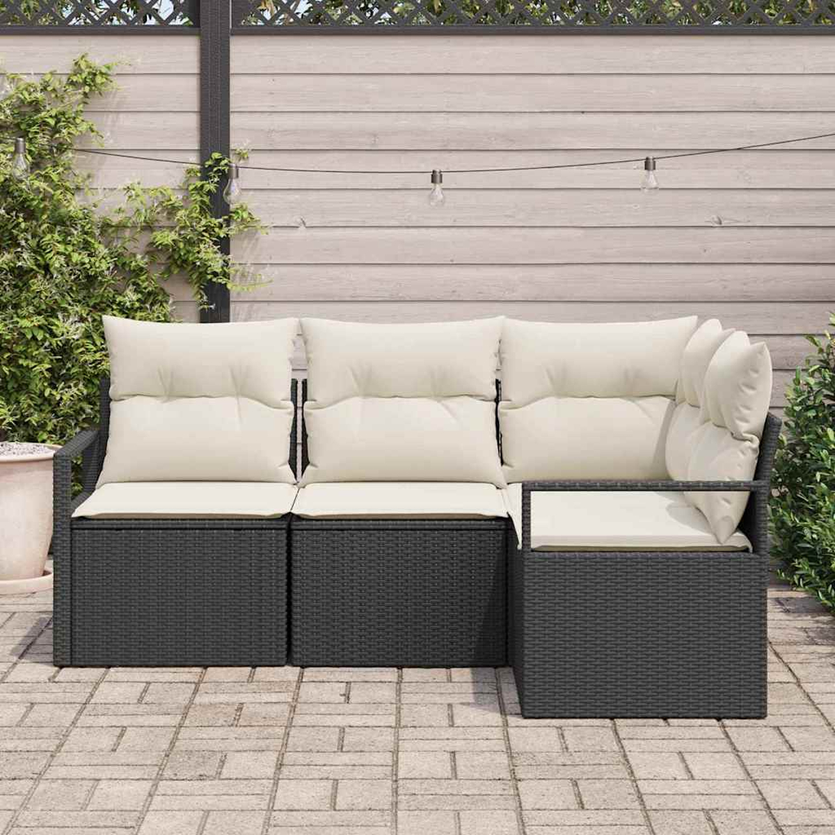 Outdoor-Ecksofa mit cremefarbenen Kissen. Dunkle Korbbasis auf einer Terrasse. Holzzaun und Grün im Hintergrund.