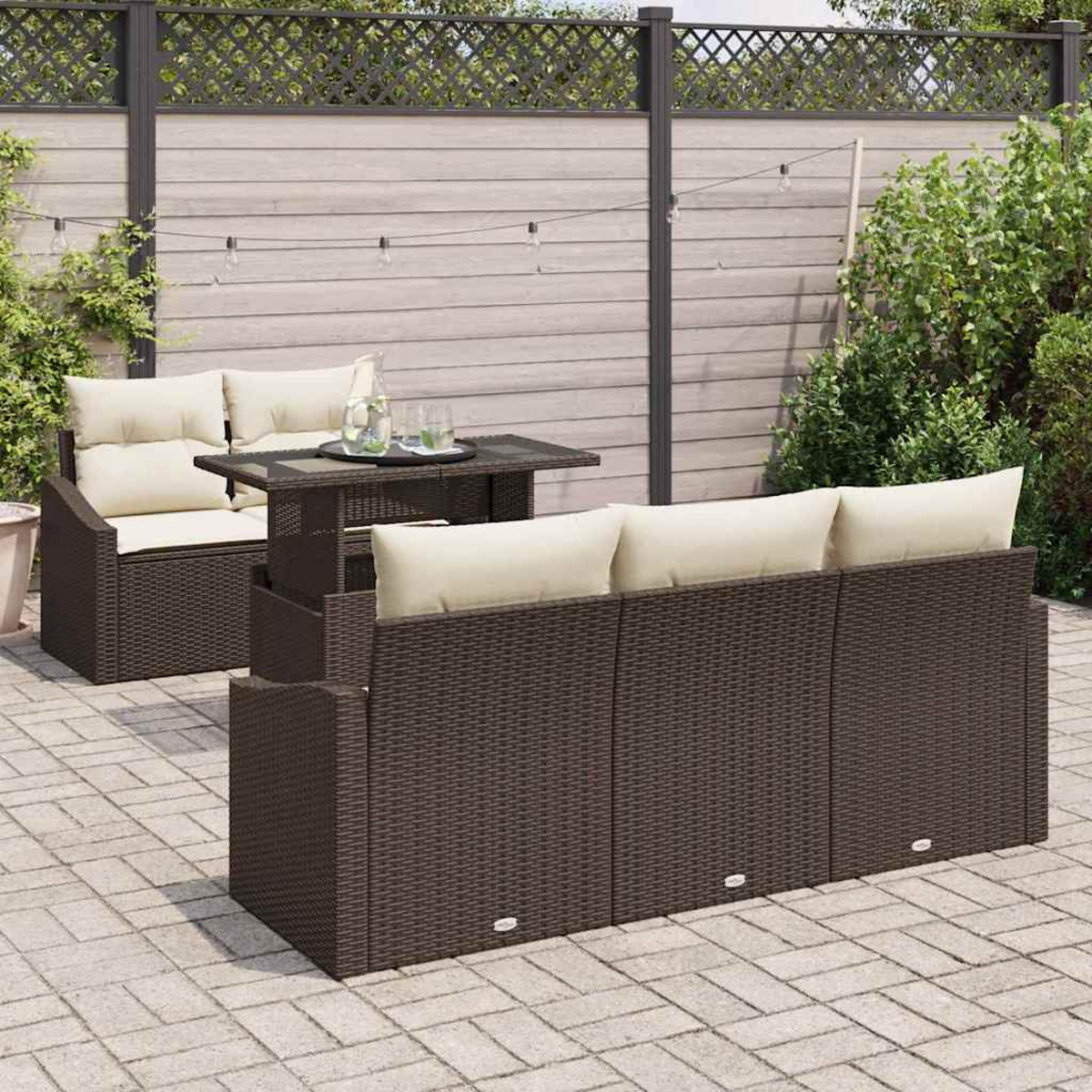Gartenmöbel-Set mit braunem Korbmöbel-Sofa, Tisch und Stühlen mit cremefarbenen Kissen. Auf einer Ziegelterrasse mit Holzzaun.