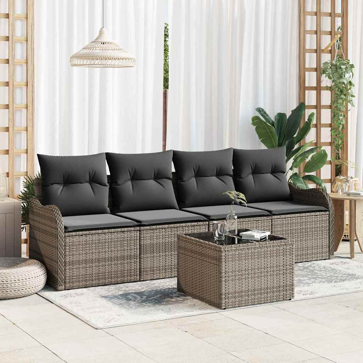 Garten-Sitzgruppe mit grauen Kissen, Korbgewebe und quadratischem Couchtisch. Auf einem Teppich vor weißen Vorhängen.