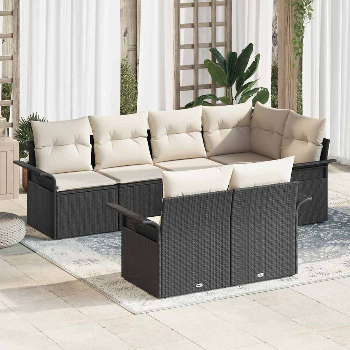 Gartenmöbel-Set mit dunkelgrauen Korbflechtrahmen und cremefarbenen Kissen. Das Set steht auf einem Teppich, im Hintergrund weiße Vorhänge.
