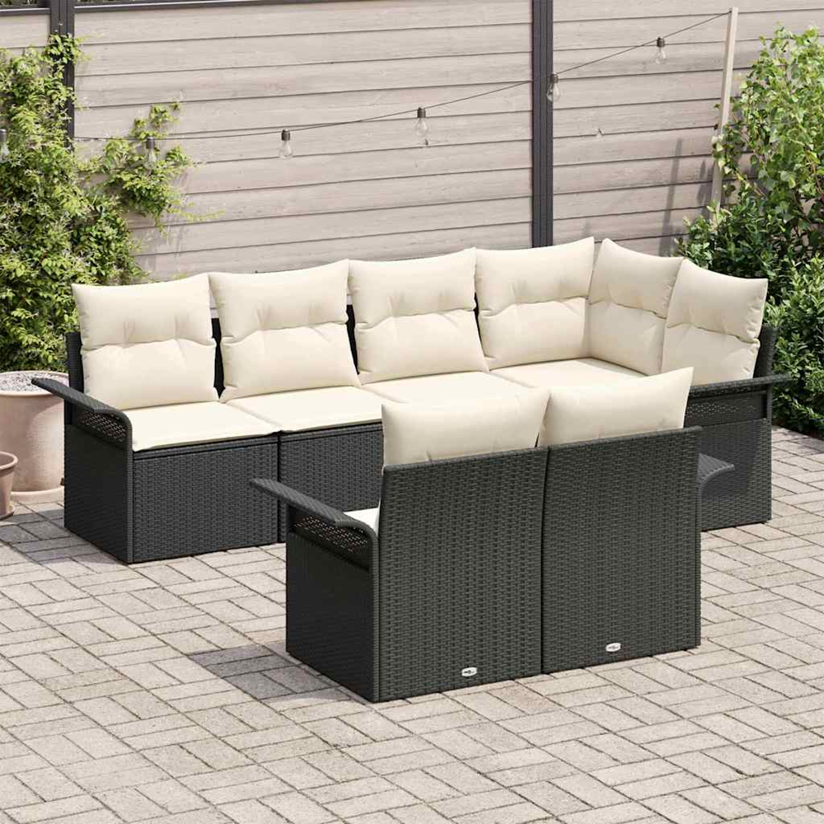 Garten-Sitzgruppe mit dunkelgrauen Korbmöbeln und cremefarbenen Kissen. Das Set umfasst ein Ecksofa und zwei Sessel auf einer Steinpflasterterrasse.