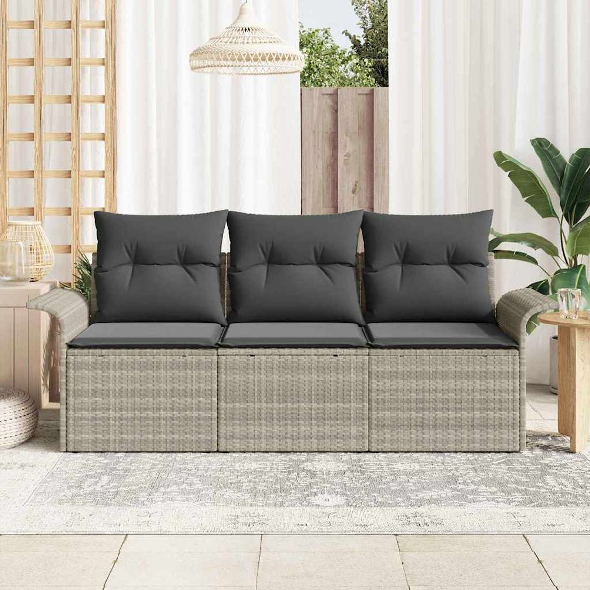 Geflochtenes Outdoor-Sofa mit grauen Kissen. Vorhänge, Pflanzen und eine Hängelampe sind im Hintergrund. Teppich auf dem Boden.