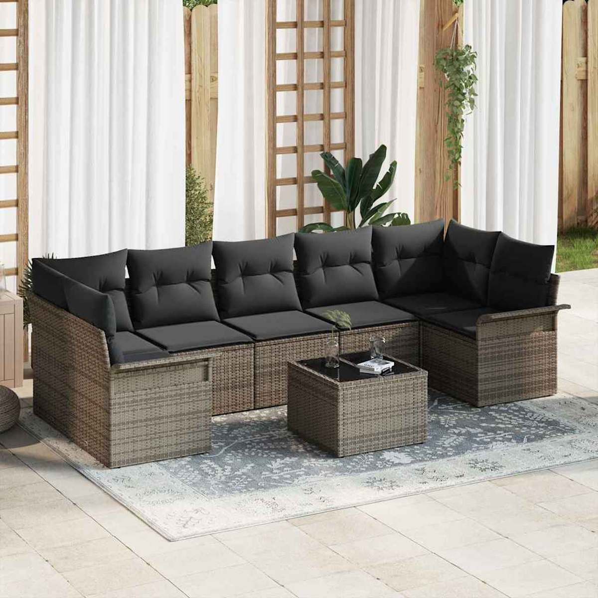 Outdoor-Ecksofa mit schwarzen Kissen und einem Couchtisch auf einem gemusterten Teppich, vor weißem Vorhang und Holzzaun.