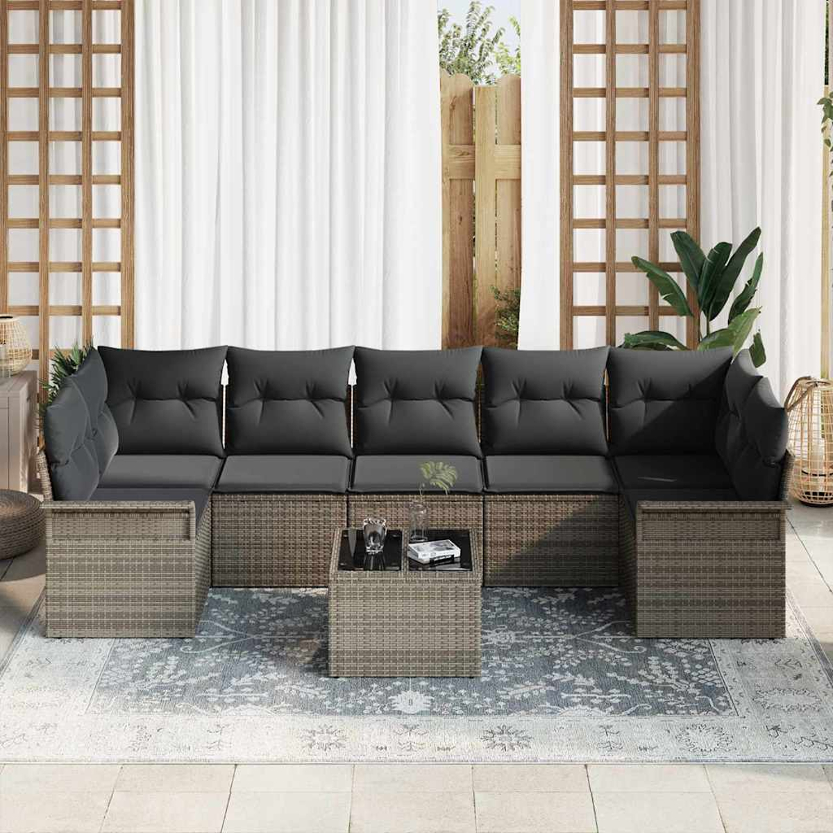 Outdoor-Ecksofa mit grauen Kissen, einem kleinen Tisch und einem gemusterten Teppich. Weiße Vorhänge und Holzgitter im Hintergrund.