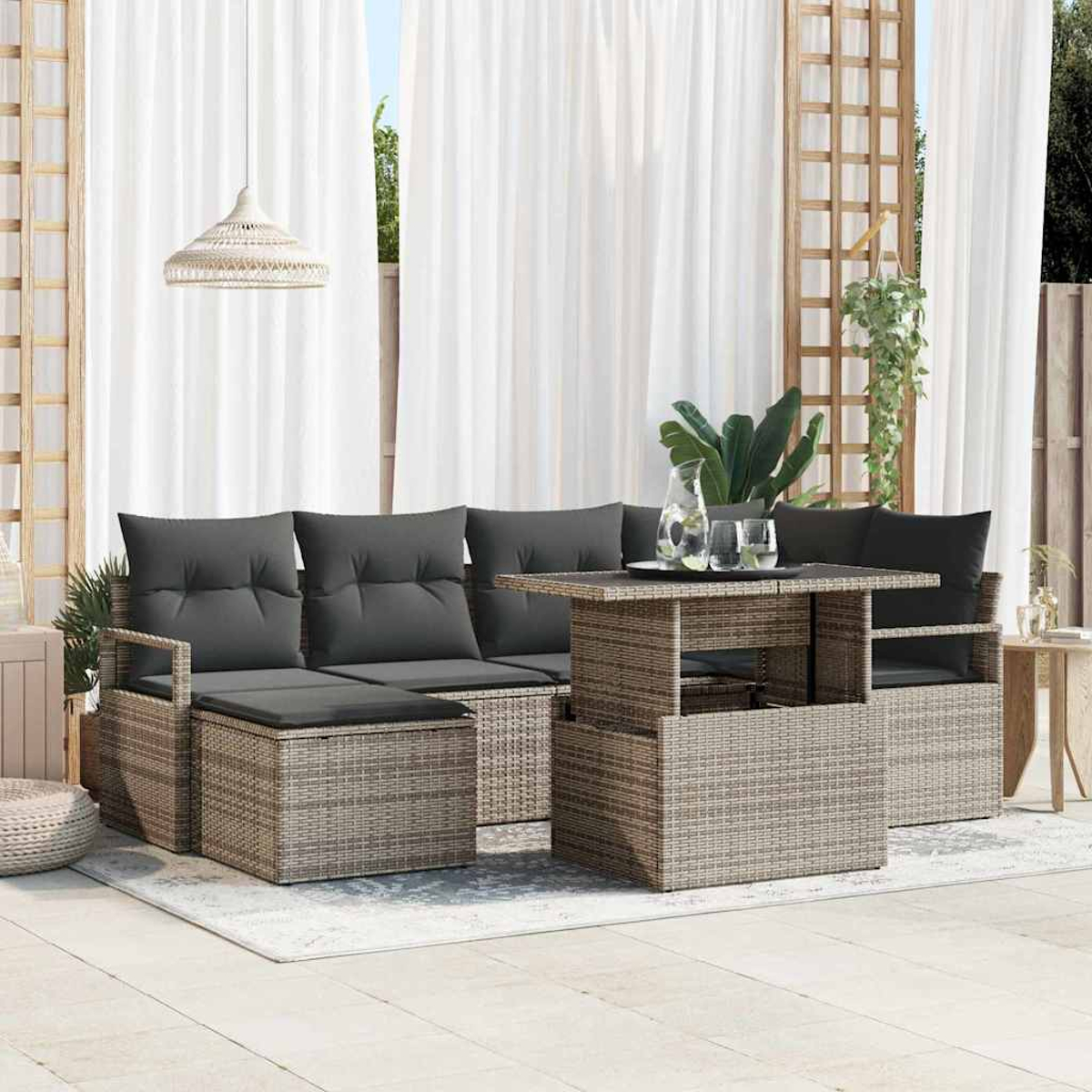 Terrassenset mit grauen Kissen, Korbmöbeln, Tisch und weißen Vorhängen im Hintergrund. Pflanzen und eine Hängelampe sind sichtbar.