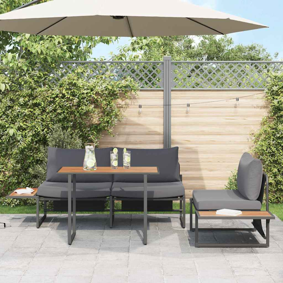 Terrassenset im Freien mit grauen Kissen, Holztisch und großem Sonnenschirm. Enthält Getränke, Pflanzen und einen Holzzaun im Hintergrund.
