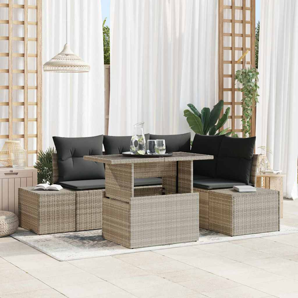 Sitzbereich im Freien mit Korbmöbeln. Ein Tisch, zwei Sofas mit schwarzen Kissen und weiße Vorhänge sind sichtbar.