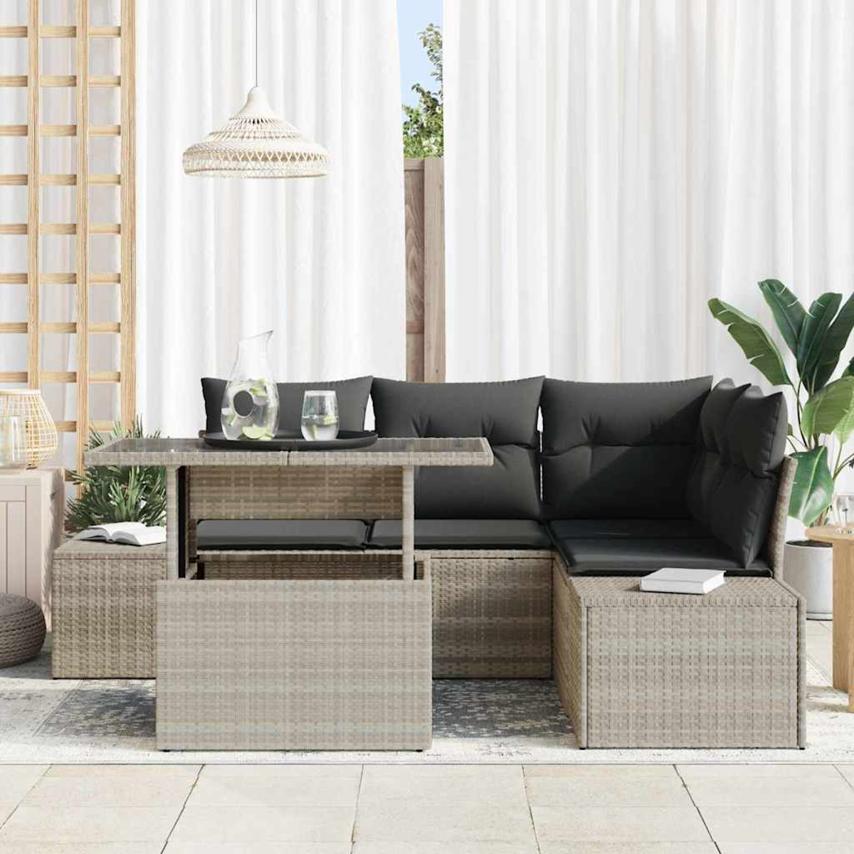 Terrassenset im Freien mit grauen Kissen, Glastisch mit Wasser und Krug sowie einer Hängeleuchte. Weiße Vorhänge im Hintergrund.