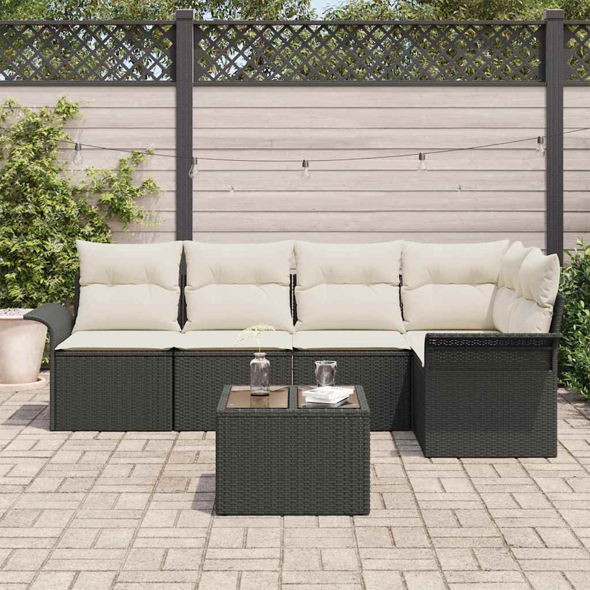 Outdoor-Sitzgruppe mit dunkelgrauem Korbgeflecht, cremefarbenen Kissen und einem kleinen Tisch auf einer Backstein-Terrasse. Im Hintergrund ist ein Zaun.