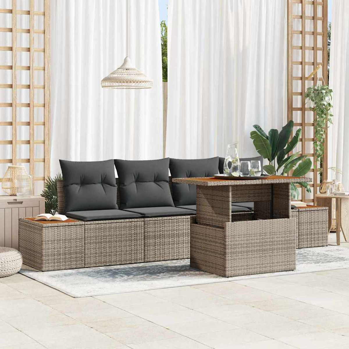 Juego de asientos al aire libre: sofá de mimbre con cojines grises, mesa elevable y mesas auxiliares en un patio con cortinas transparentes.