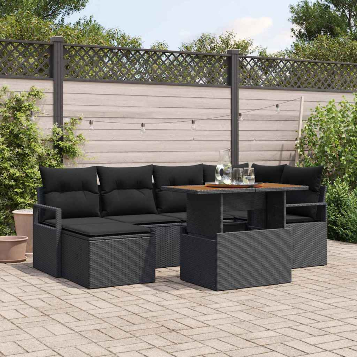 Gartenmöbel-Set: schwarzes Korbmöbel, Couchtisch und Kissen. Holzzaun und Pflanzen im Hintergrund.