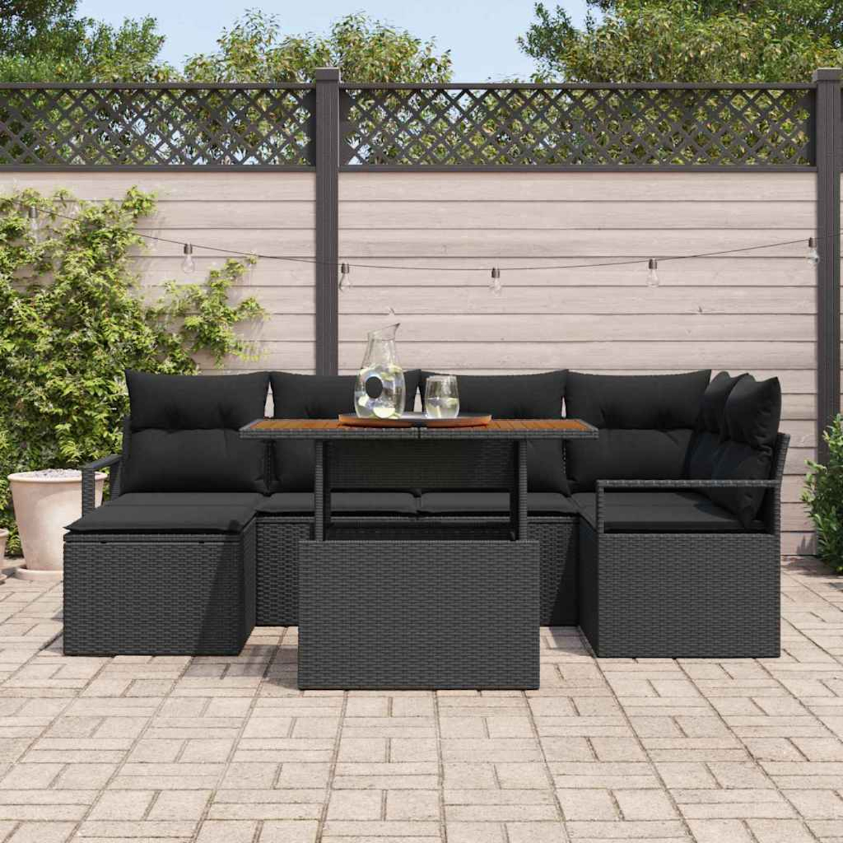 Schwarzes Outdoor-Korbmöbel-Set mit Kissen, einem Couchtisch und dekorativem Zaun im Hintergrund. Getränke auf dem Tisch.
