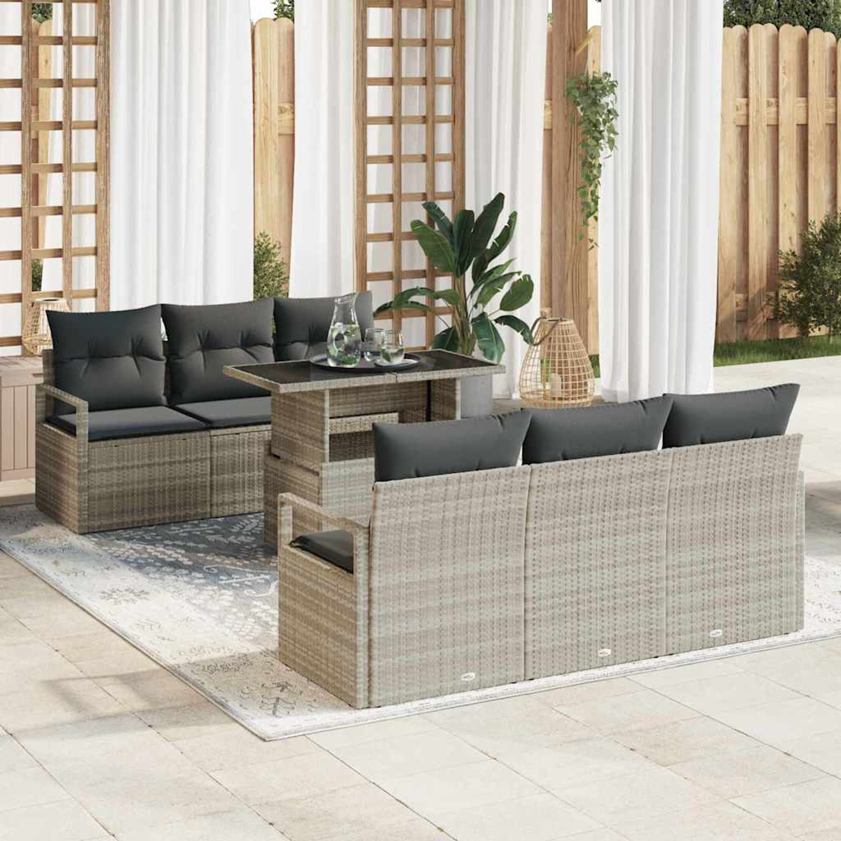 Garten-Terrassenset mit grauen Kissen. Verfügt über einen Tisch, zwei Sofas und einen Teppich. Weiße Vorhänge und Holzzaun im Hintergrund.