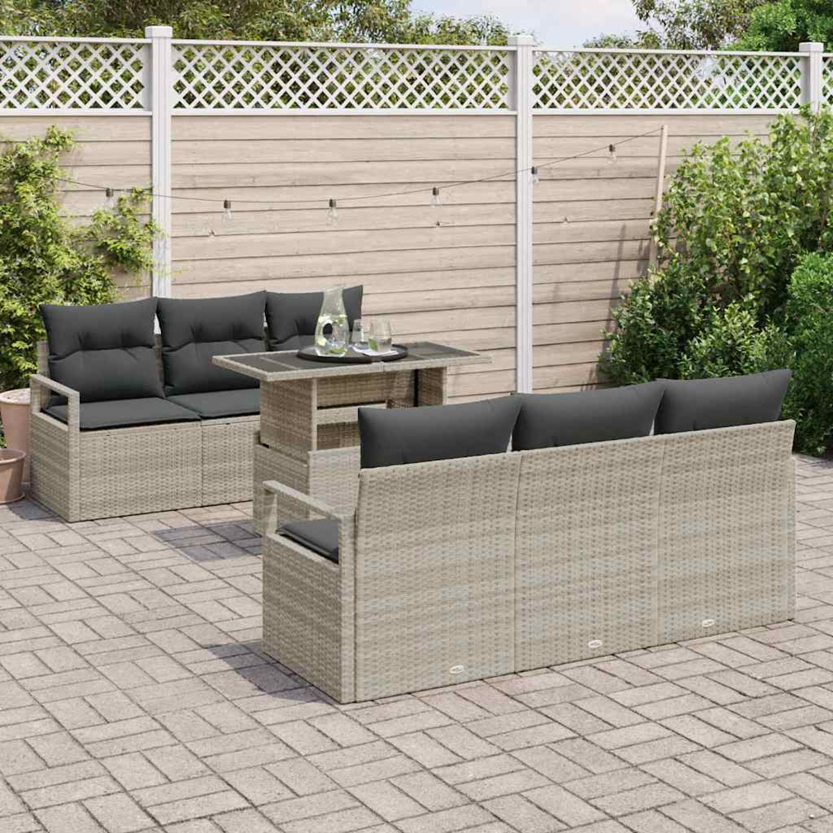 Garten-Set mit Rattangeflechtmöbeln, dunkelgrauen Kissen und einem Tisch. Im Hintergrund ein Holzzaun und Grün.