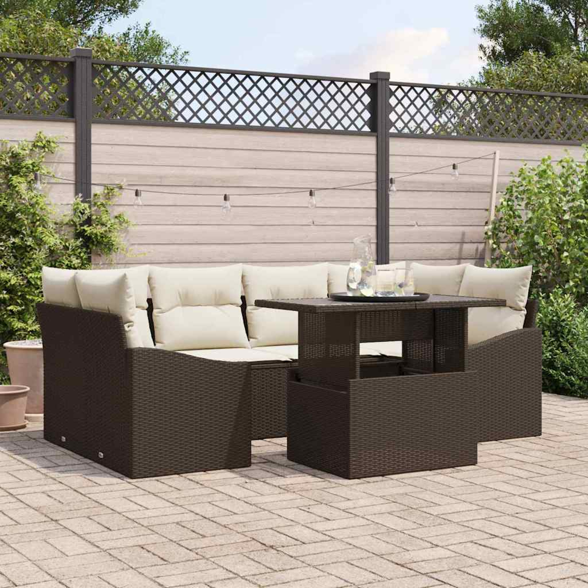 Outdoor-Terrassenset mit braunen Korbmöbeln und cremefarbenen Kissen. Enthält einen Tisch mit Gläsern und einer Kanne. Der Hintergrund ist ein Holzzaun.