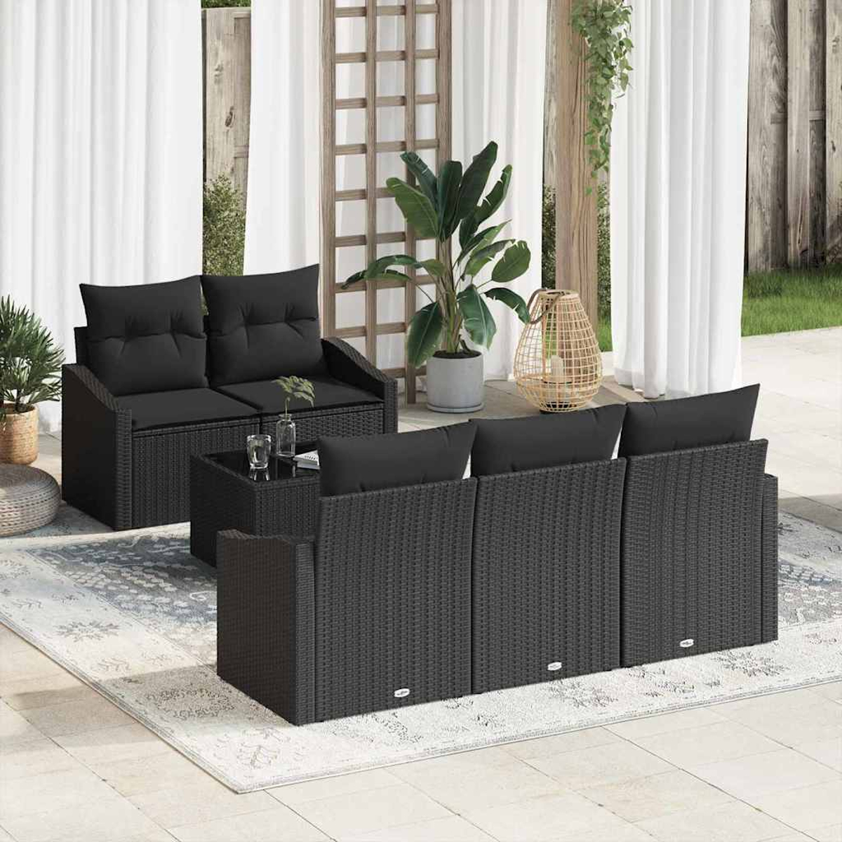 Gartenmöbel-Set: schwarzes Korbmöbel-Set mit schwarzen Kissen, auf hellem Teppich mit Pflanzen und Vorhängen.