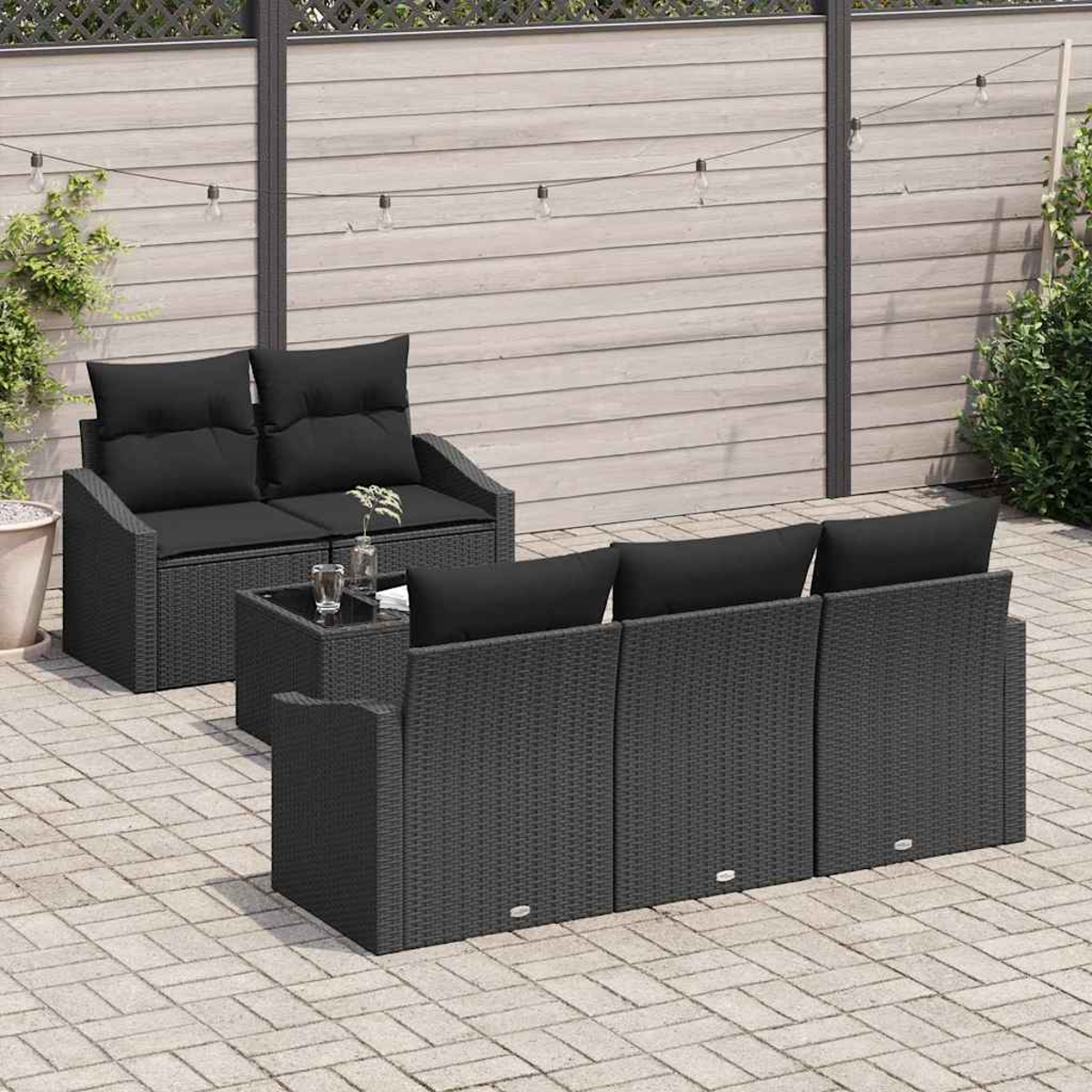 Gartenmöbel-Set. Dunkelgraues Korbmöbel-Sofa, Stühle mit schwarzen Kissen, kleiner Tisch. Holzzaun und Lichterkette im Hintergrund.