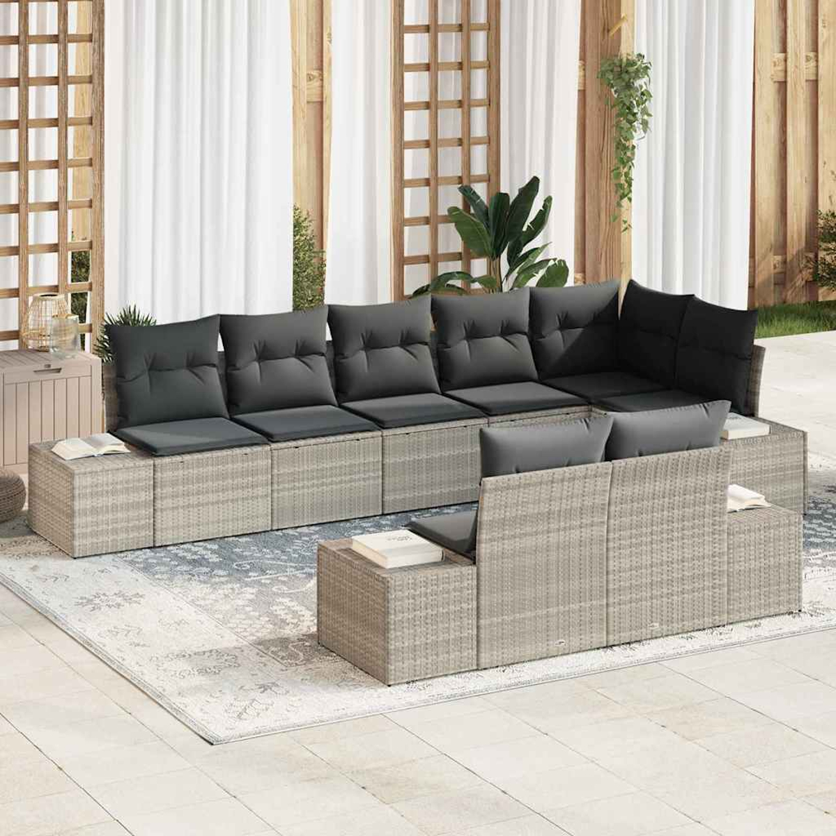 Sofá seccional para exteriores con cojines grises. Muebles de mimbre beige sobre una alfombra estampada, contra paneles de madera y cortinas blancas.