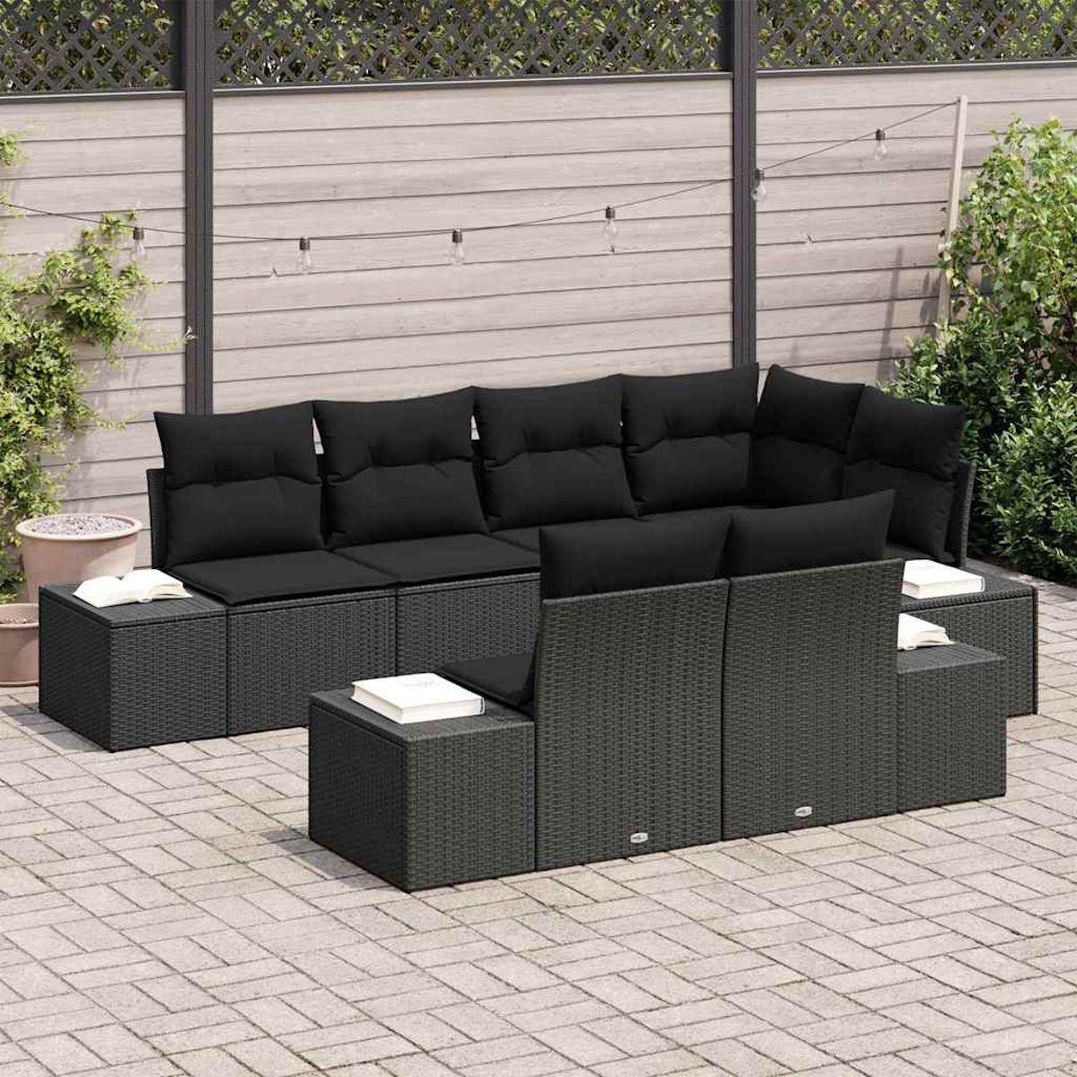 Schwarzes Rattan-Sofa-Set für den Außenbereich mit schwarzen Kissen. Bücher liegen auf den Beistelltischen. Der Hintergrund zeigt einen Holzzaun und Pflanzen.