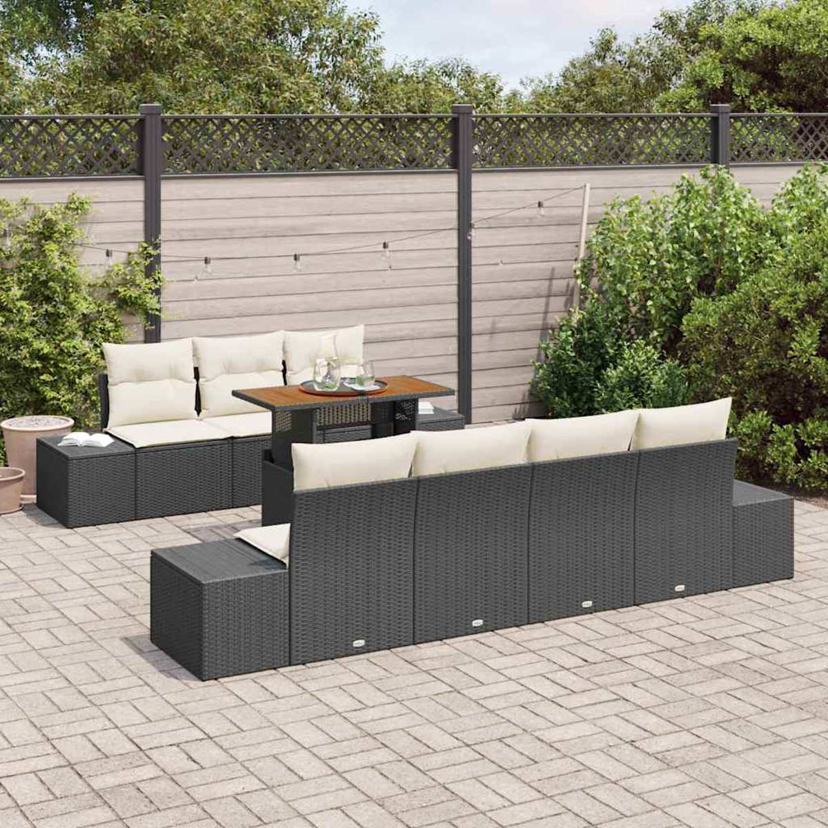 Garten-Terrassenset mit grauen Korbmöbeln, beigefarbenen Kissen, einem Holztisch und einer Backsteinterrasse. Im Hintergrund befinden sich ein Zaun und Grün.