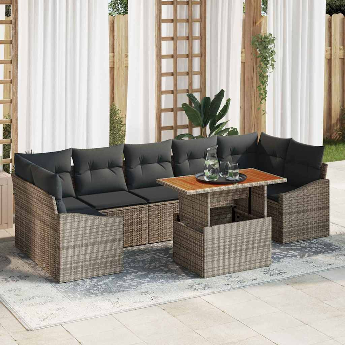 Gartenmöbel-Set aus Korbgeflecht mit grauen Kissen, einem Holztisch und weißen Vorhängen im Hintergrund. Eine Kanne und Gläser stehen auf dem Tisch.