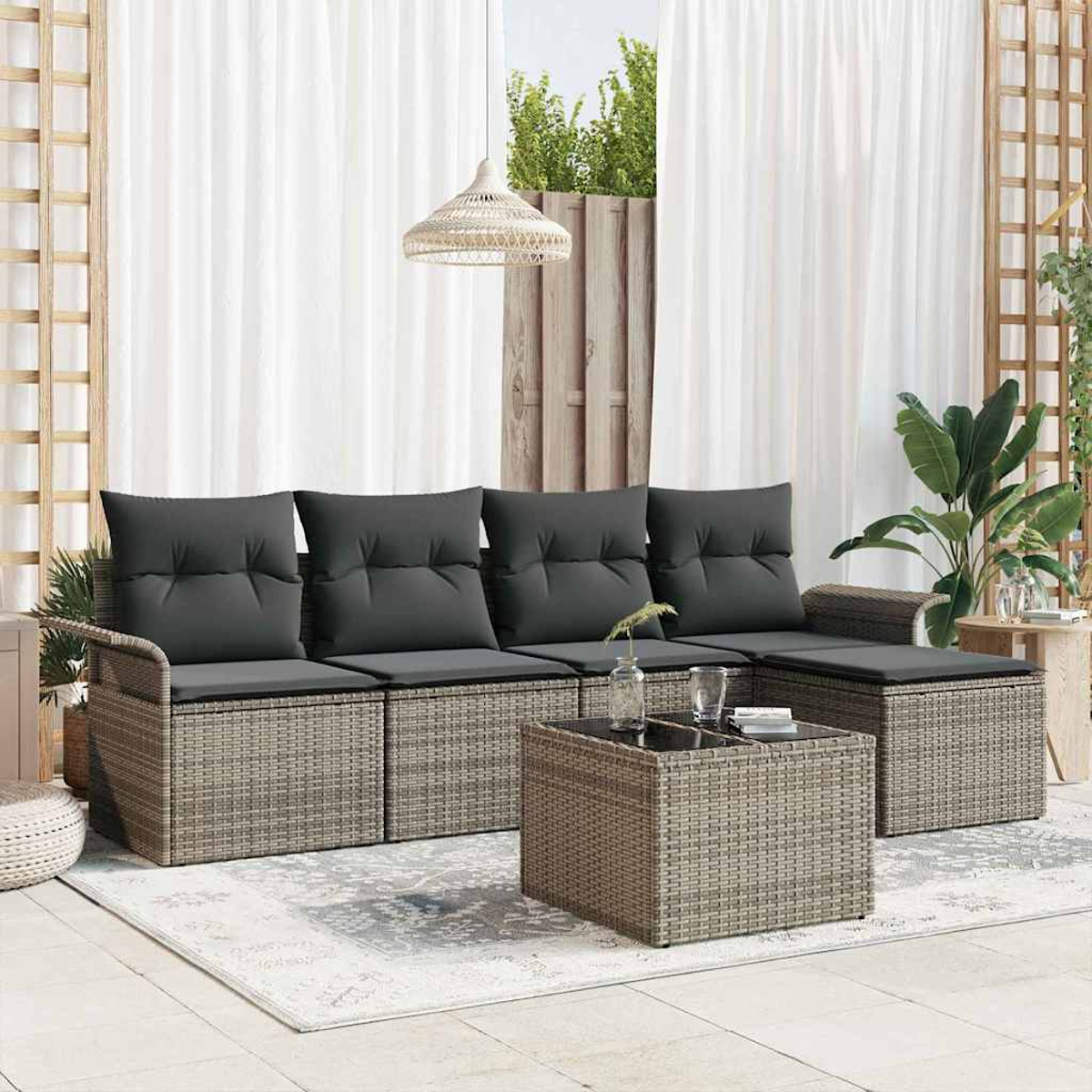 Rattan-Sofa im Freien mit grauen Kissen und Couchtisch. Vorhänge und Pflanzen im Hintergrund. Eine gemütliche Umgebung im Freien.