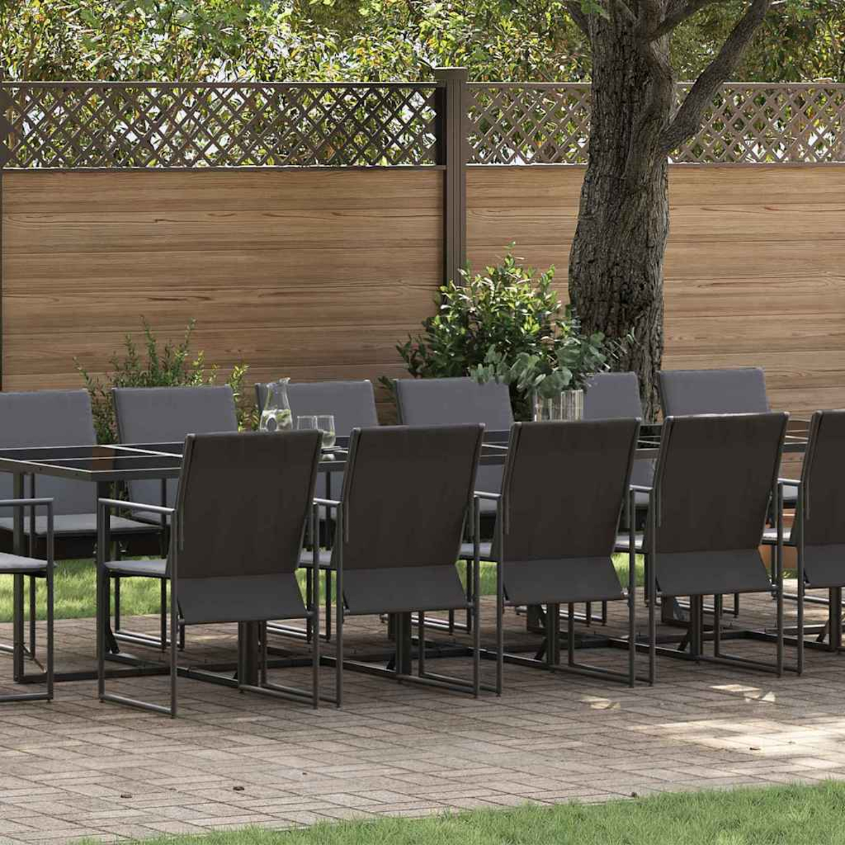 Essgruppe im Freien mit Tisch und Stühlen auf einer Ziegelterrasse, Holzzaun und Baum im Hintergrund.