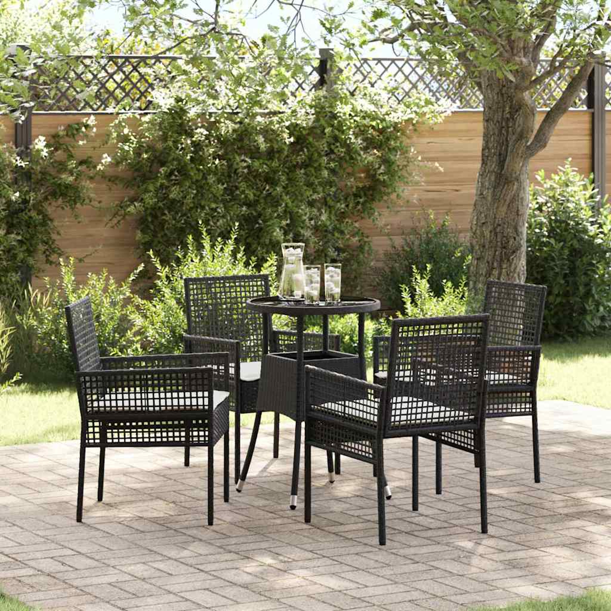 Garten-Set: schwarze Stühle, kleiner Tisch mit Wasser und Gläsern, auf einer Ziegelterrasse. Grüne Büsche und ein Baum im Hintergrund.