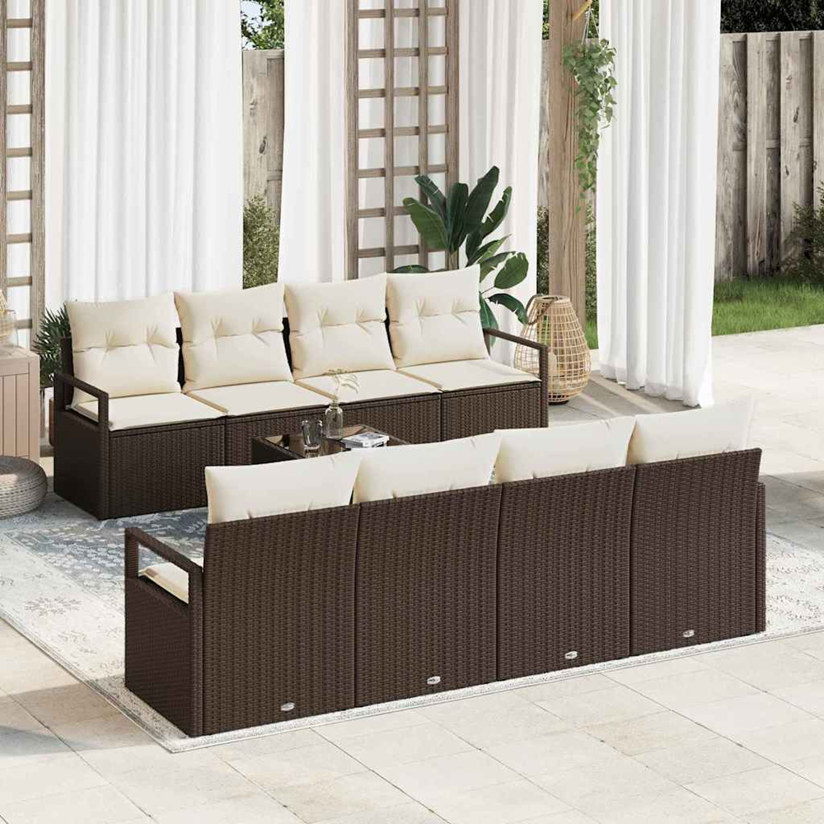 Terrassen-Set mit braunen Korbsesseln, beigen Kissen und einem Tisch mit Glasplatte. Weiße Vorhänge und eine Pflanze im Hintergrund.