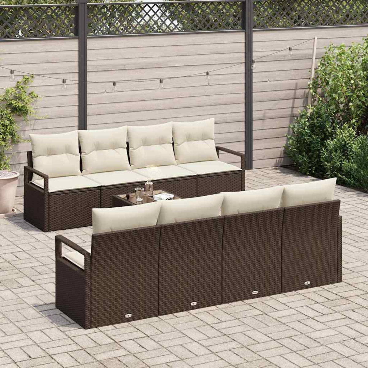 Terrassenmöbel: zwei braune Korbs Sofas mit cremefarbenen Kissen, ein Glastisch und eine Backsteinterrasse. Hintergrund: Holzzaun und Pflanzen.