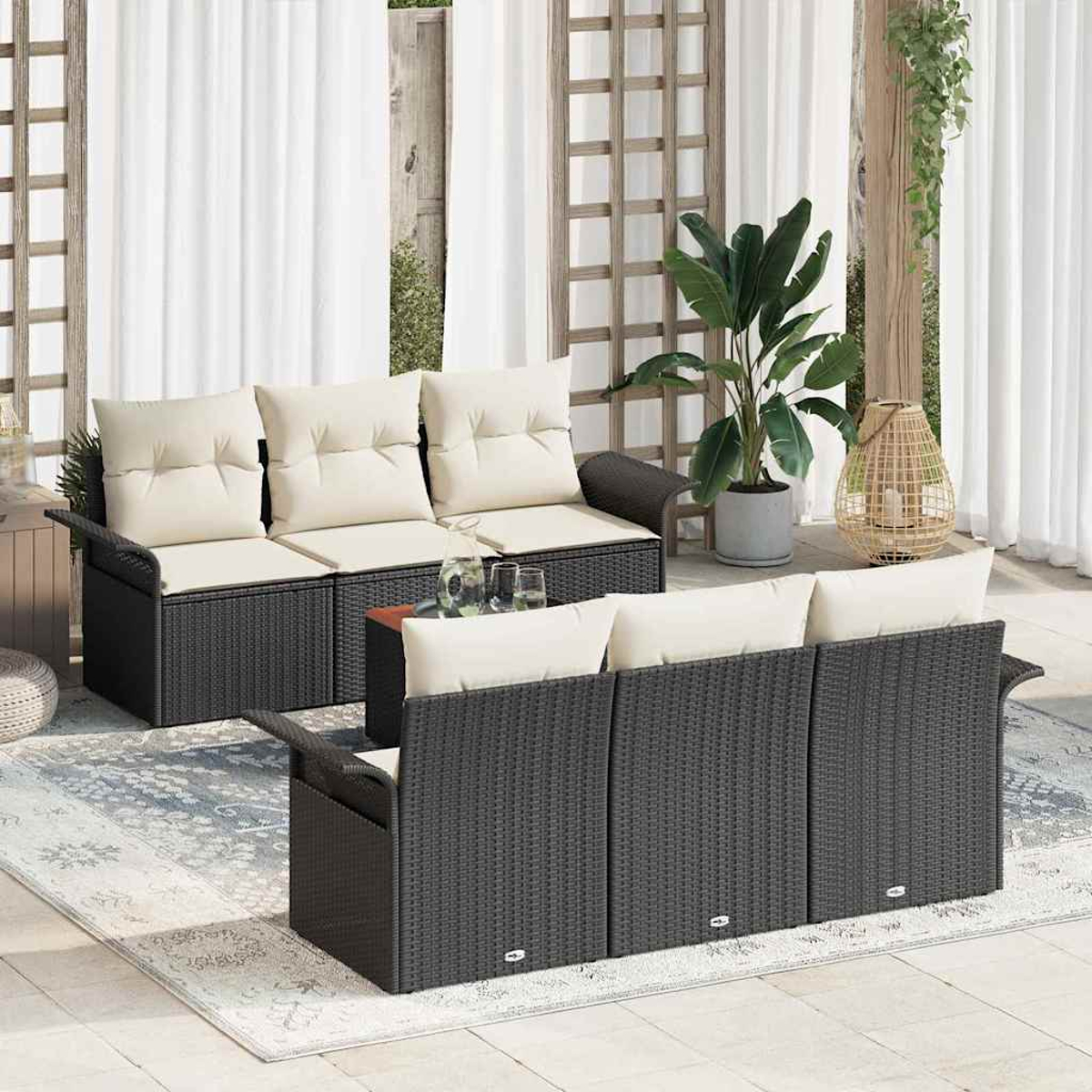 Szene im Freien mit schwarzen Rattansofas, beigen Kissen, kleinem Tisch, Topfpflanze und Laterne. Weiße Vorhänge im Hintergrund.
