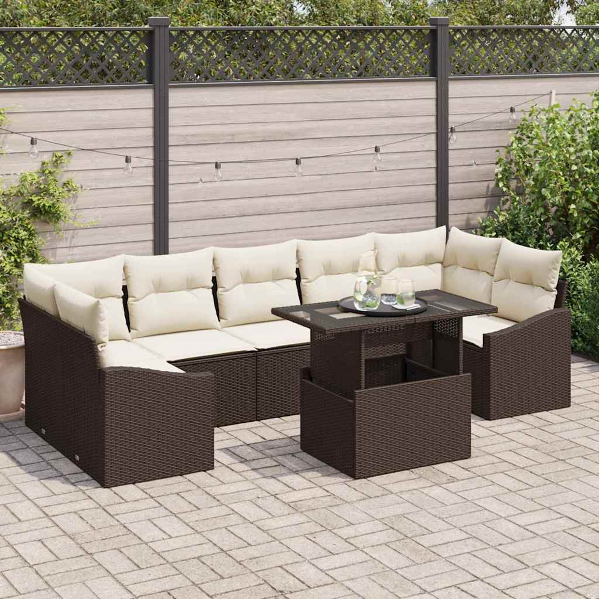 Garten-Terrassenset mit braunen Korbmöbeln, beigefarbenen Kissen und einem Tisch mit Glasplatte. Die Szene spielt auf einer Ziegelterrasse mit Zaun.