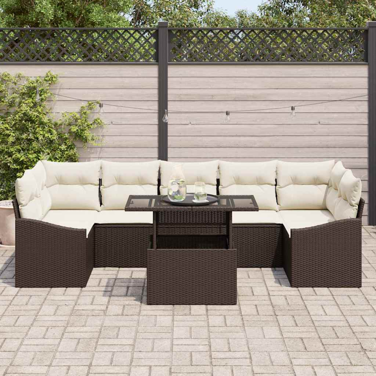 Geflochtenes Outdoor-Ecksofa mit cremefarbenen Kissen, Glastisch und hellem Zaun im Hintergrund.