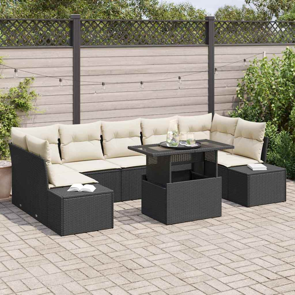 Schwarzes Outdoor-Korbsessel-Sofa mit cremefarbenen Kissen und einem Tisch mit Hubtisch auf einer Ziegelstein-Terrasse. Ein Holzzaun und Grün im Hintergrund.