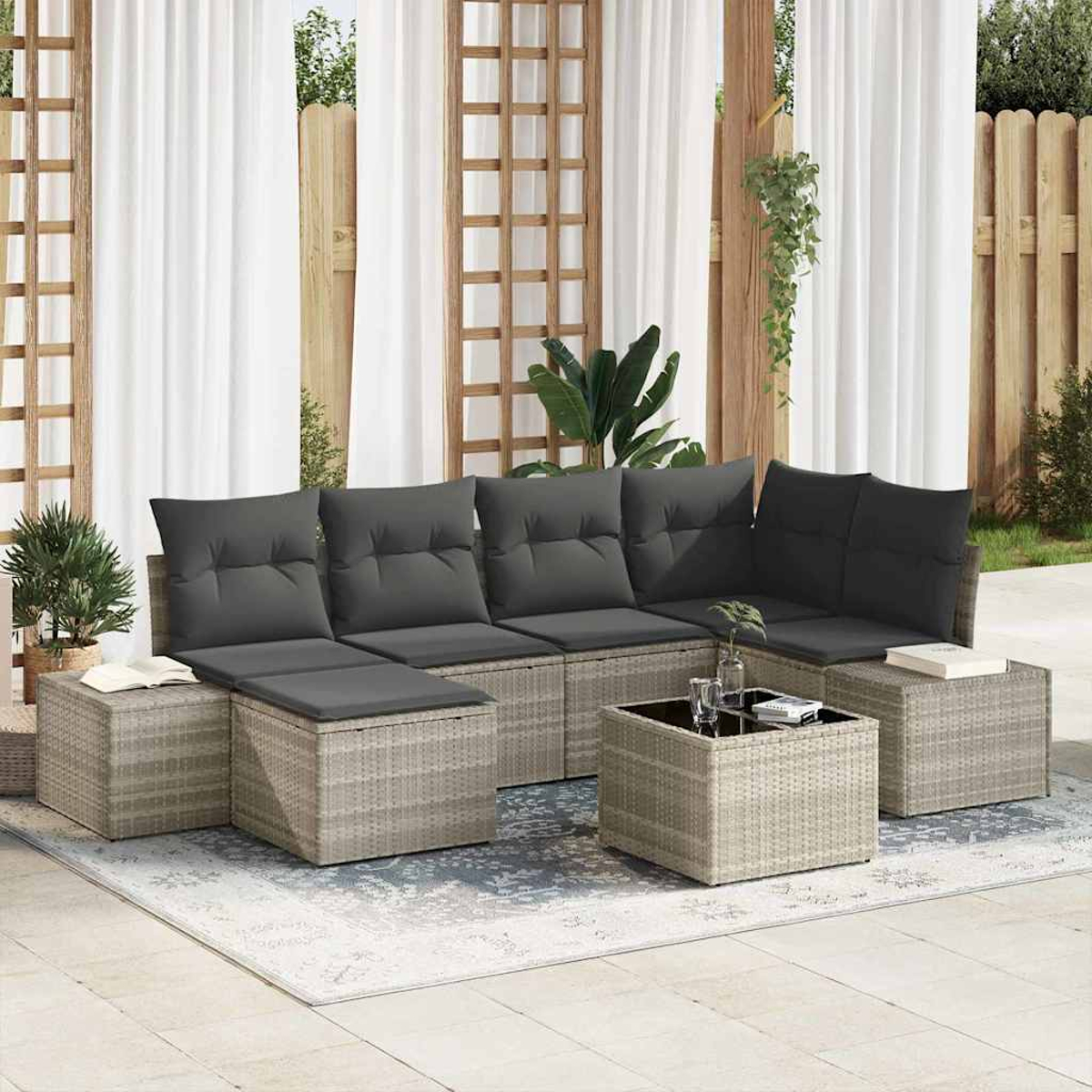 Garten-Sitzgruppe mit grauen Kissen, einem Couchtisch und Ottomanen auf einem gemusterten Teppich. Weiße Vorhänge und ein Holzgitter im Hintergrund.